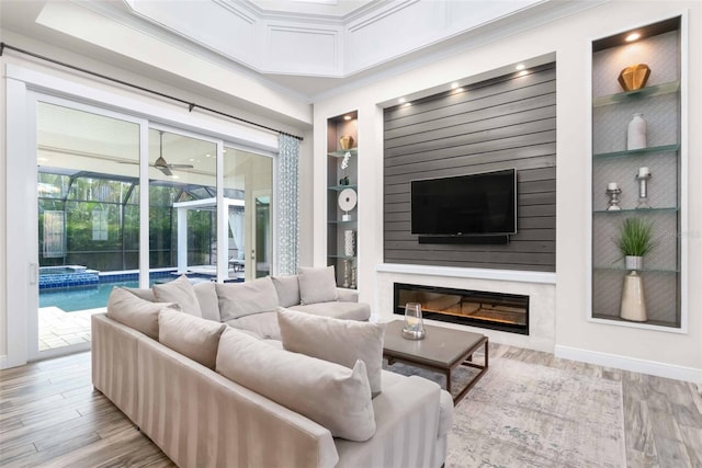 living room featuring built in shelves, ceiling fan, light hardwood / wood-style flooring, and crown molding