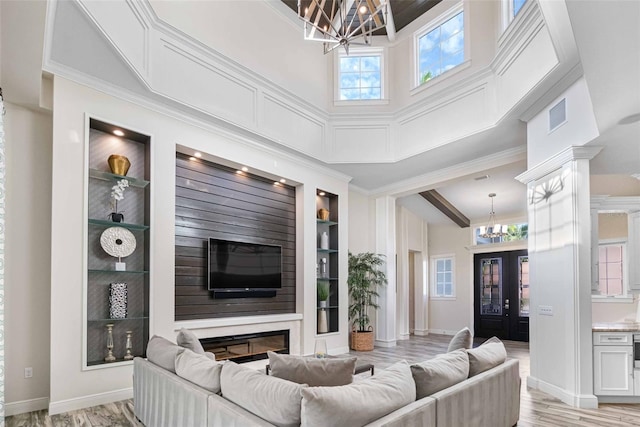 living room featuring an inviting chandelier, light hardwood / wood-style flooring, built in shelves, ornamental molding, and a towering ceiling