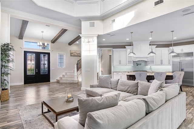 living room featuring sink, french doors, an inviting chandelier, beamed ceiling, and a towering ceiling