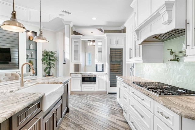 kitchen featuring stainless steel appliances, light stone counters, decorative light fixtures, white cabinets, and custom exhaust hood