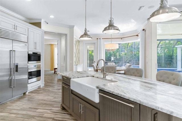 kitchen with pendant lighting, sink, ornamental molding, appliances with stainless steel finishes, and white cabinetry