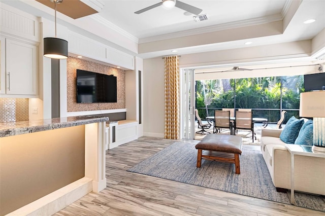 living room with light hardwood / wood-style flooring, a raised ceiling, ceiling fan, and crown molding