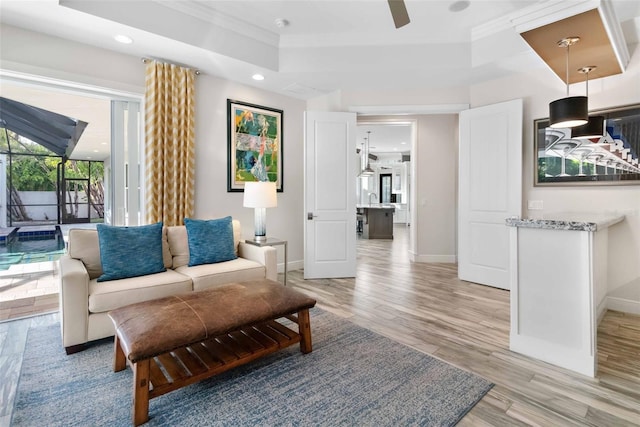 living room with light hardwood / wood-style floors, a raised ceiling, and ornamental molding