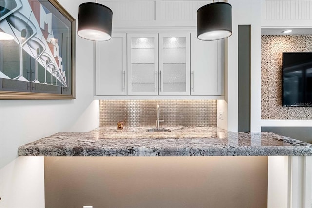 kitchen featuring tasteful backsplash, light stone counters, sink, decorative light fixtures, and white cabinets