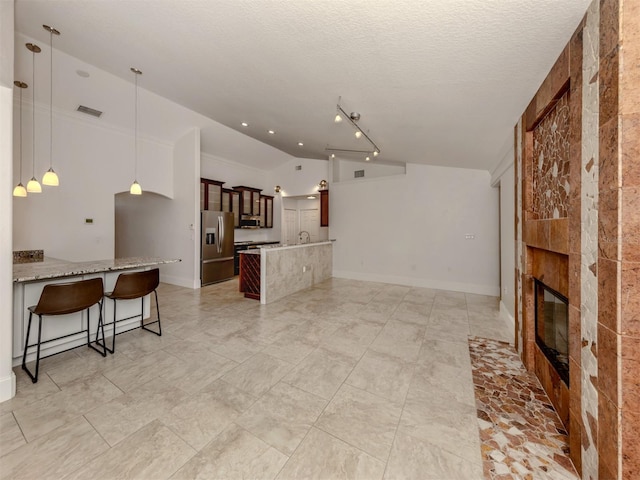 kitchen with kitchen peninsula, stainless steel fridge, a kitchen breakfast bar, a fireplace, and vaulted ceiling