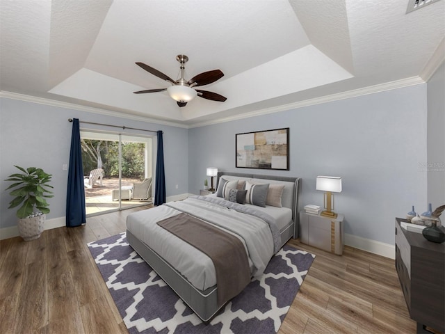 bedroom with wood-type flooring, access to exterior, ceiling fan, a tray ceiling, and crown molding