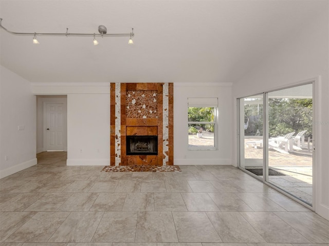 unfurnished living room featuring a tile fireplace, crown molding, and track lighting