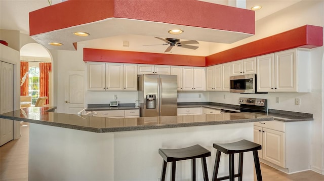 kitchen featuring light hardwood / wood-style floors, a kitchen bar, white cabinetry, appliances with stainless steel finishes, and ceiling fan