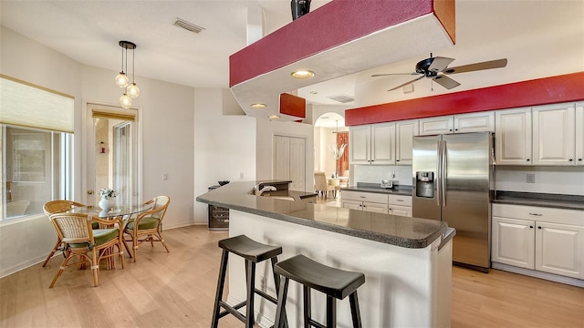 kitchen with white cabinetry, a kitchen breakfast bar, ceiling fan, stainless steel refrigerator with ice dispenser, and pendant lighting