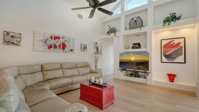 living room with high vaulted ceiling, ceiling fan, built in shelves, and light hardwood / wood-style flooring