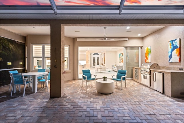 patio terrace at dusk featuring an outdoor kitchen, ceiling fan, and area for grilling