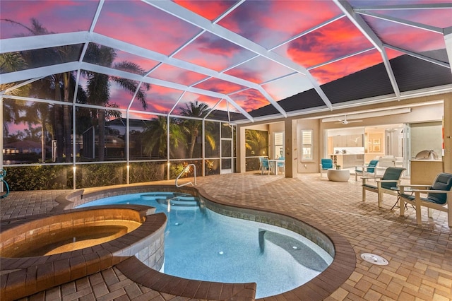 pool at dusk with exterior kitchen, a patio area, glass enclosure, and an in ground hot tub