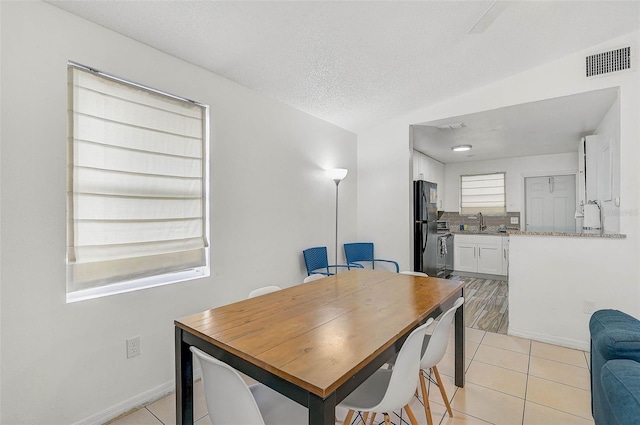 dining space with a textured ceiling, lofted ceiling, light tile patterned floors, and sink