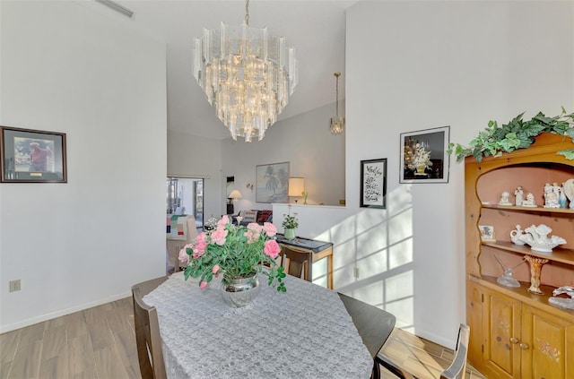 dining space with a notable chandelier, a towering ceiling, and light wood-type flooring