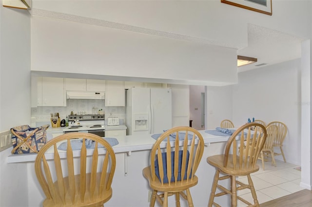 kitchen with a kitchen bar, kitchen peninsula, white cabinets, white appliances, and backsplash