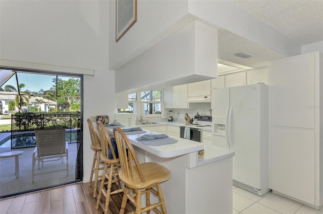 kitchen featuring white appliances, white cabinetry, a healthy amount of sunlight, a kitchen bar, and kitchen peninsula