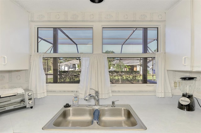 kitchen with a wealth of natural light, sink, a textured ceiling, and white cabinets