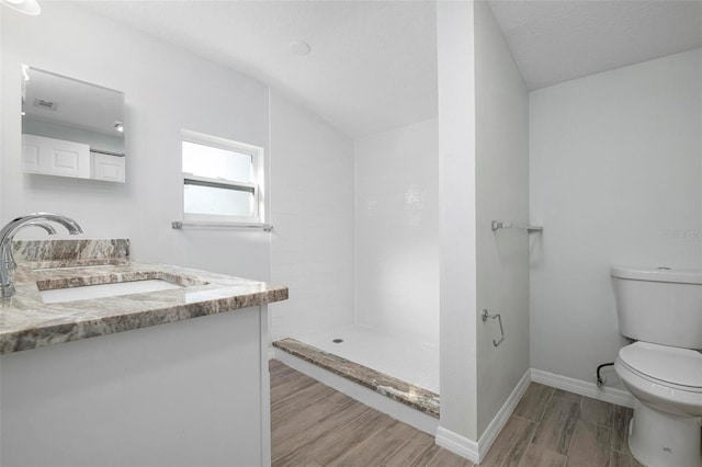 bathroom with baseboards, toilet, wood finished floors, a tile shower, and vanity