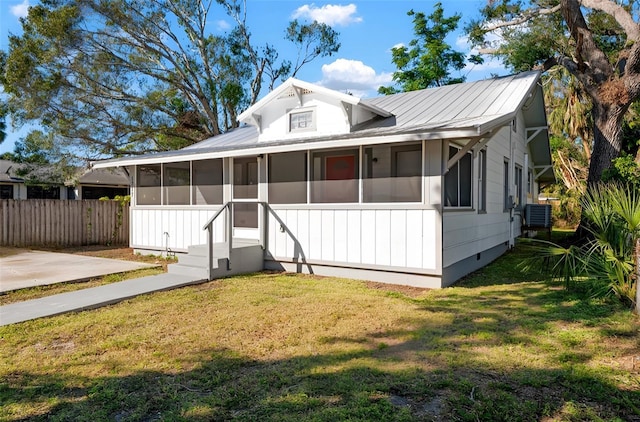 view of front of house with metal roof, central AC unit, fence, a sunroom, and a front yard