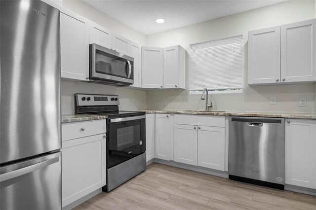 kitchen with recessed lighting, a sink, white cabinetry, appliances with stainless steel finishes, and light wood finished floors