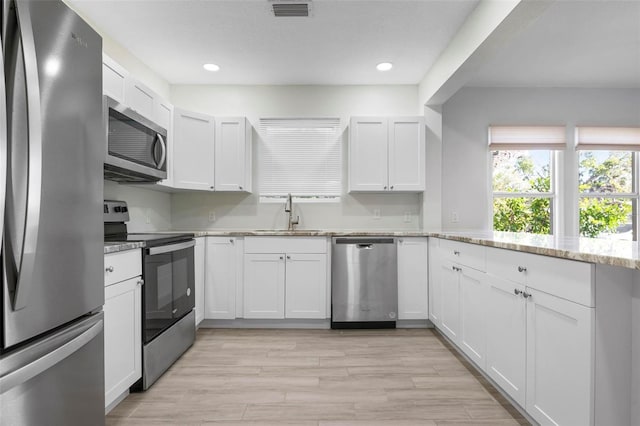 kitchen featuring stainless steel appliances, a sink, white cabinetry, visible vents, and light stone countertops