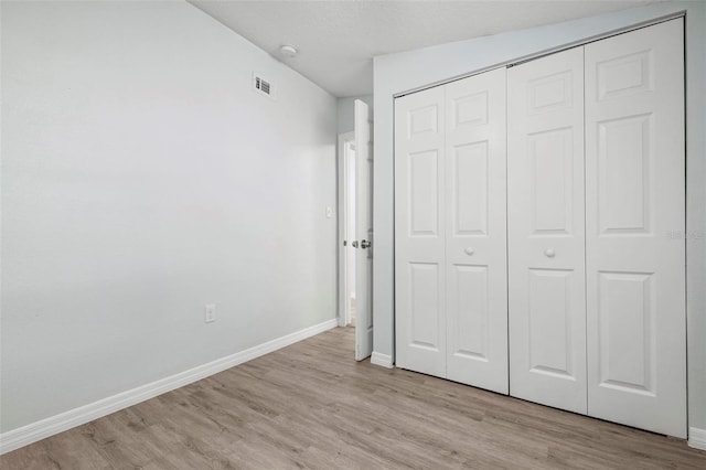 unfurnished bedroom featuring a textured ceiling, light wood finished floors, a closet, and baseboards