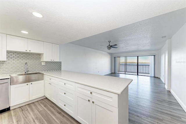 kitchen with sink, stainless steel dishwasher, kitchen peninsula, a textured ceiling, and white cabinets