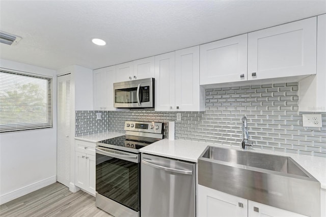 kitchen with appliances with stainless steel finishes, light wood-type flooring, backsplash, sink, and white cabinets