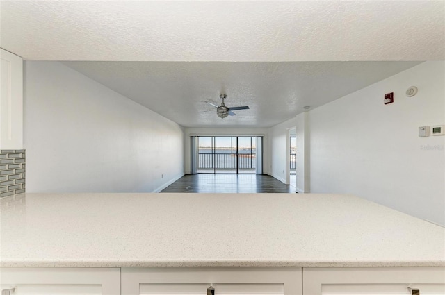 kitchen featuring a textured ceiling, tasteful backsplash, white cabinetry, and ceiling fan