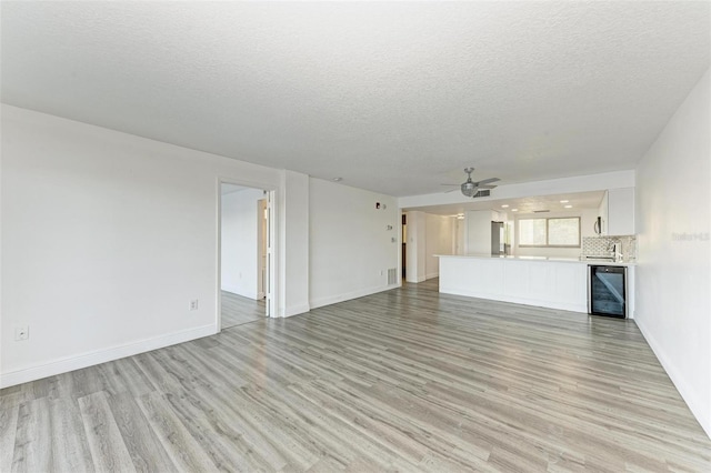 unfurnished living room with ceiling fan, light hardwood / wood-style floors, a textured ceiling, and beverage cooler