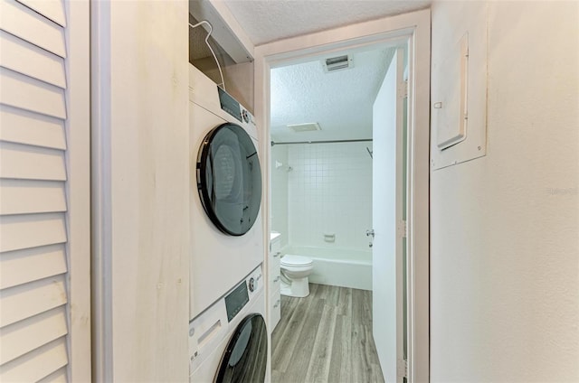 clothes washing area with electric panel, light hardwood / wood-style flooring, stacked washer / drying machine, and a textured ceiling