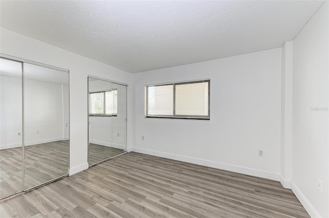 unfurnished bedroom with a textured ceiling, hardwood / wood-style flooring, and multiple closets