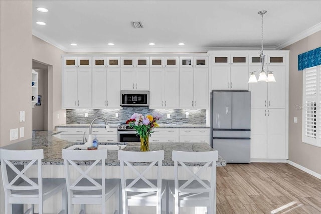 kitchen with light stone countertops, pendant lighting, a breakfast bar area, white cabinets, and appliances with stainless steel finishes