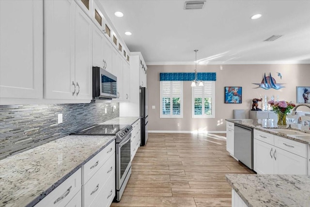 kitchen featuring appliances with stainless steel finishes, pendant lighting, white cabinetry, and ornamental molding