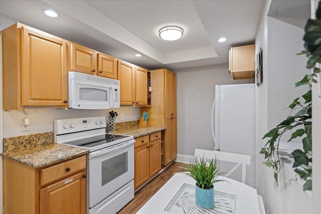 kitchen featuring white appliances, a raised ceiling, dark wood-type flooring, and light stone counters