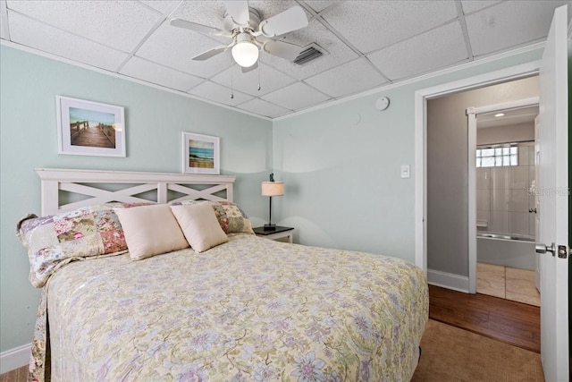 bedroom featuring carpet, a drop ceiling, ensuite bathroom, and ceiling fan