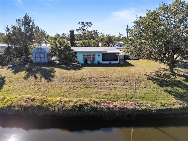 single story home with a front lawn, a water view, and a shed