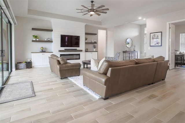 living room featuring ceiling fan, a large fireplace, and a tray ceiling