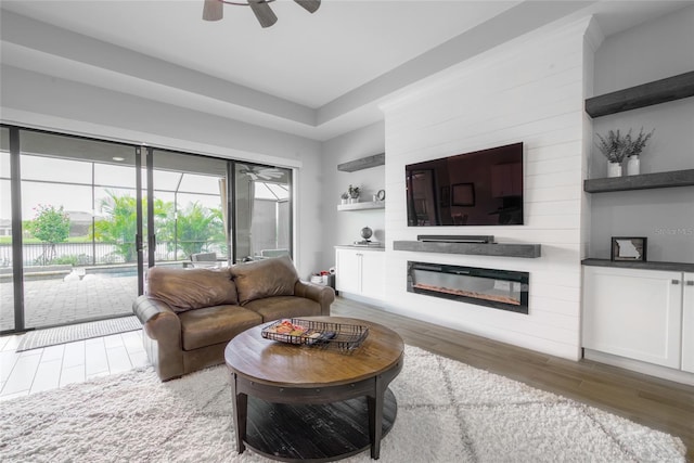 living room featuring ceiling fan, a large fireplace, and hardwood / wood-style flooring