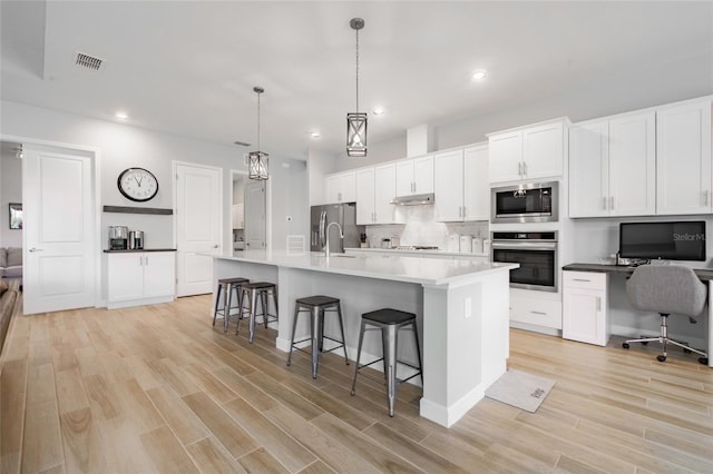 kitchen featuring white cabinetry, a kitchen bar, a center island with sink, appliances with stainless steel finishes, and decorative light fixtures