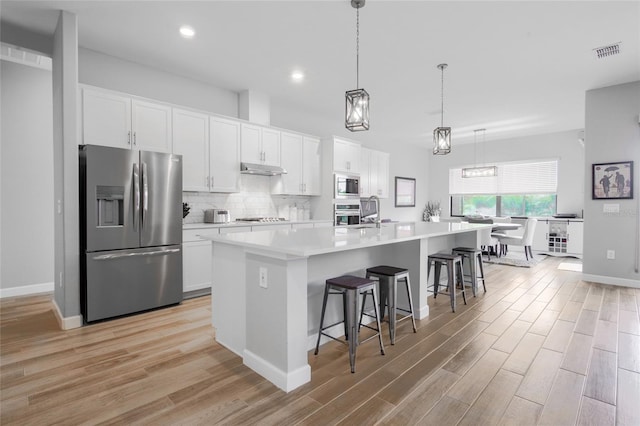 kitchen with appliances with stainless steel finishes, white cabinetry, tasteful backsplash, a kitchen breakfast bar, and a center island with sink