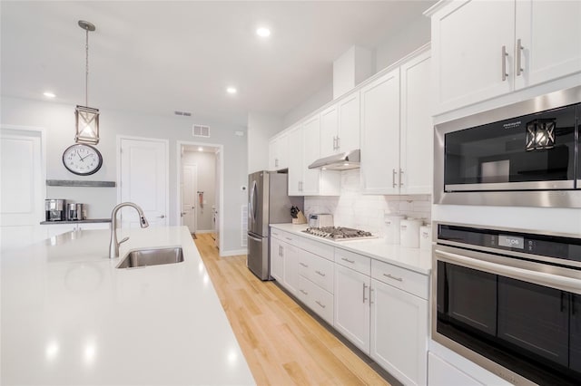 kitchen featuring pendant lighting, appliances with stainless steel finishes, white cabinetry, sink, and light wood-type flooring