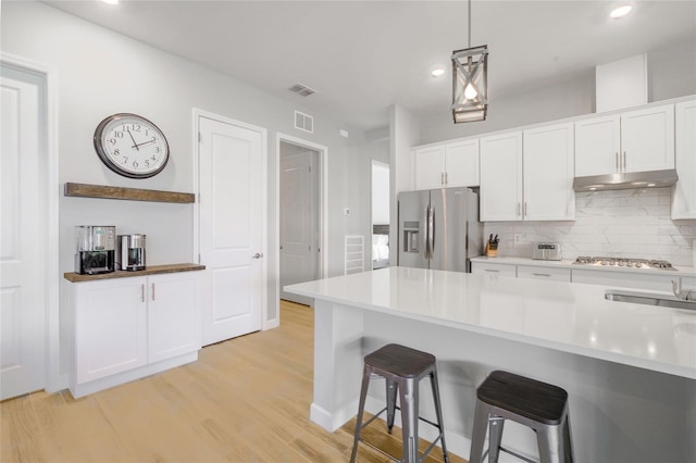 kitchen featuring appliances with stainless steel finishes, light hardwood / wood-style floors, white cabinetry, and hanging light fixtures