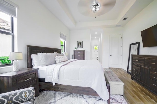 bedroom featuring ceiling fan, wood-type flooring, and a tray ceiling