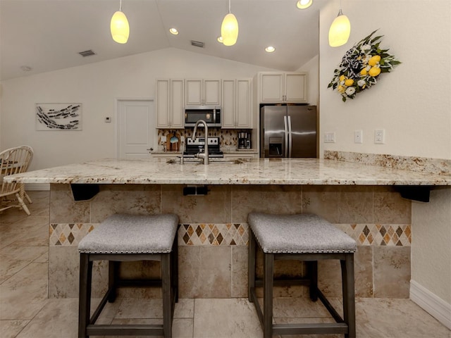 kitchen with a kitchen bar, decorative light fixtures, appliances with stainless steel finishes, and vaulted ceiling