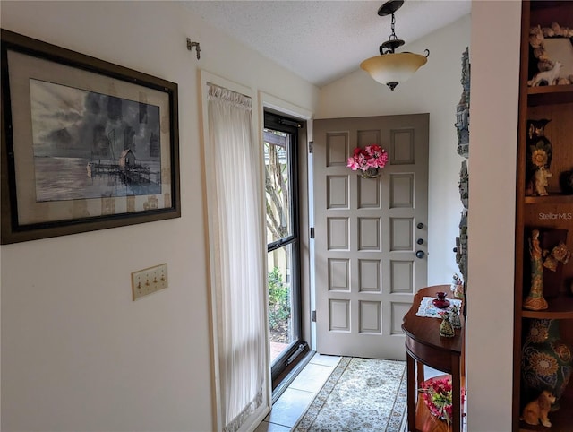 foyer with a textured ceiling, lofted ceiling, and light tile patterned flooring