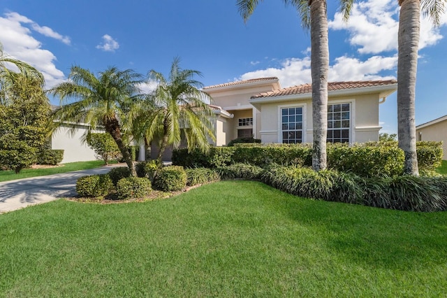 mediterranean / spanish-style home featuring stucco siding, a tiled roof, concrete driveway, and a front yard