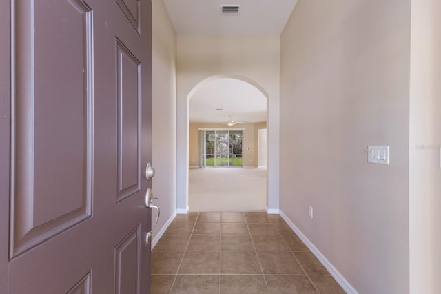 hall featuring arched walkways, visible vents, baseboards, and tile patterned floors