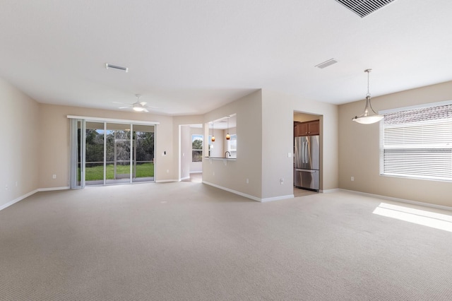 unfurnished living room with a ceiling fan, visible vents, light carpet, and baseboards