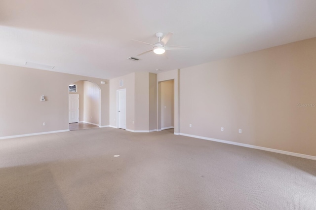 carpeted spare room with baseboards, visible vents, arched walkways, and a ceiling fan